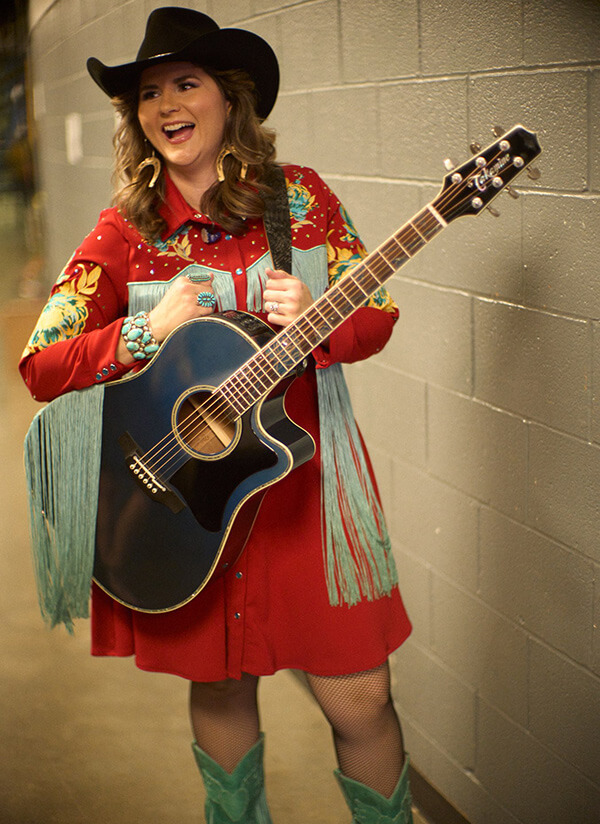 Jenee Fleenor smiling with her award outfit on and holding her guitar